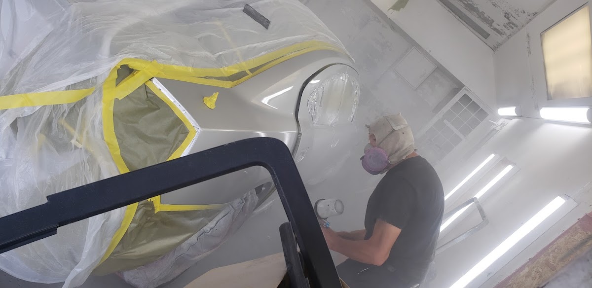 Painter in a respirator masking a car in the paint booth